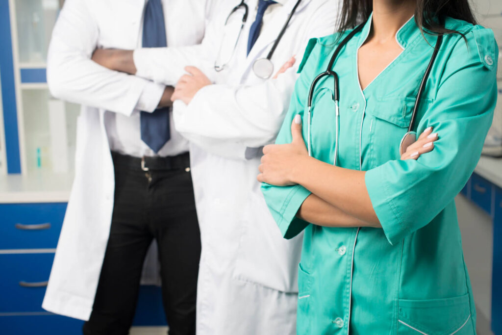 Gruppo di professionisti sanitari con camici e stetoscopi, in piedi con le braccia conserte, simbolo di collaborazione e lavoro di squadra in ambito medico.