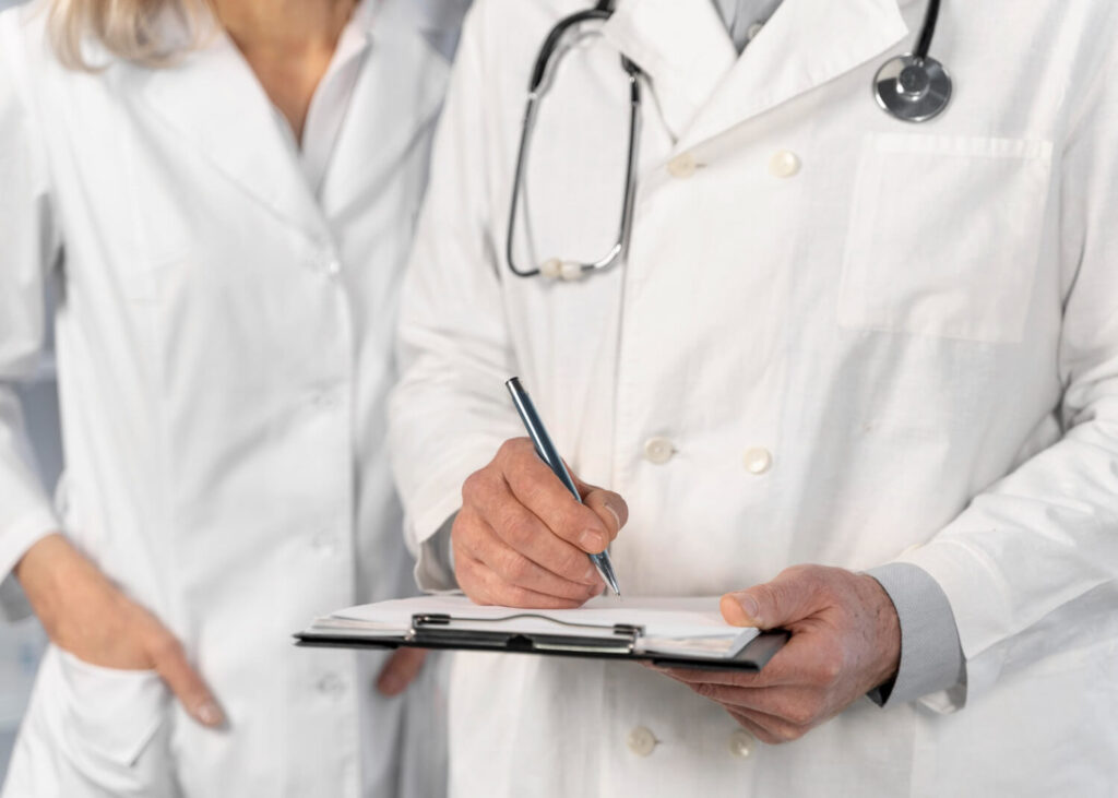 Due medici in camice bianco, uno dei quali scrive appunti su una cartella clinica, simbolo di collaborazione professionale in ambito sanitario.