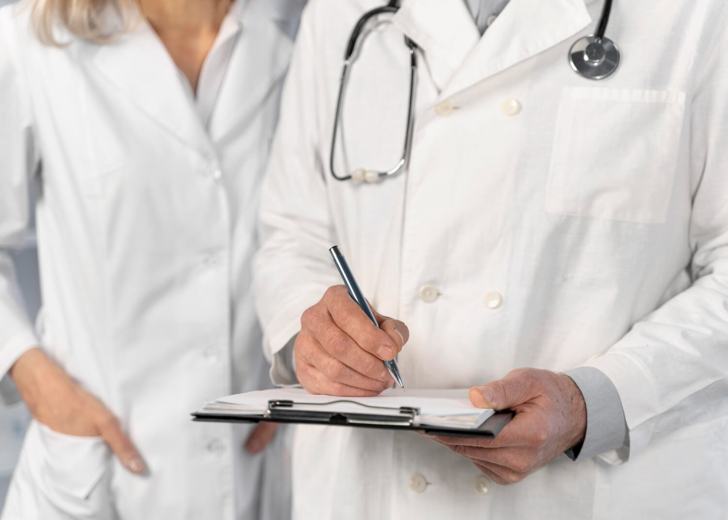 Due medici in camice bianco, uno dei quali scrive appunti su una cartella clinica, simbolo di collaborazione professionale in ambito sanitario.